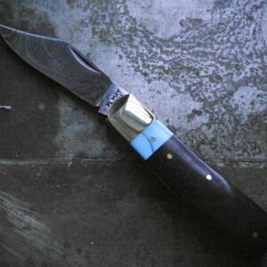 A handmade pocket knife featuring a damascus steel blade with swirled patter, paired with a handle made of ebony wood and a turquoise collar. The bolster is polished brass, giving the knife a striking and elegant appearance.